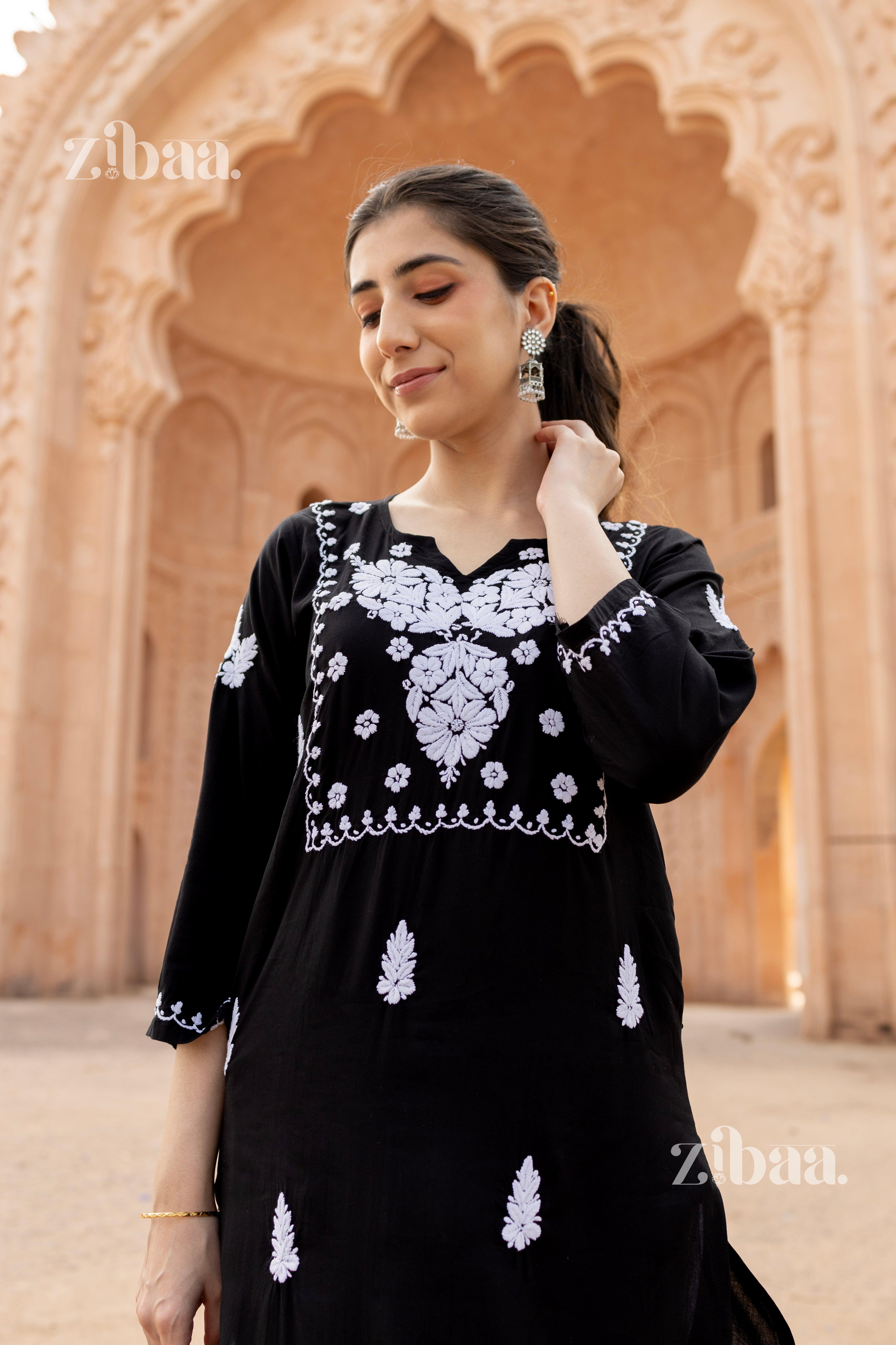 Close up photo of a girl in black Chikankari kurti with intricate white embroidery, complemented by earrings in a heritage setting.