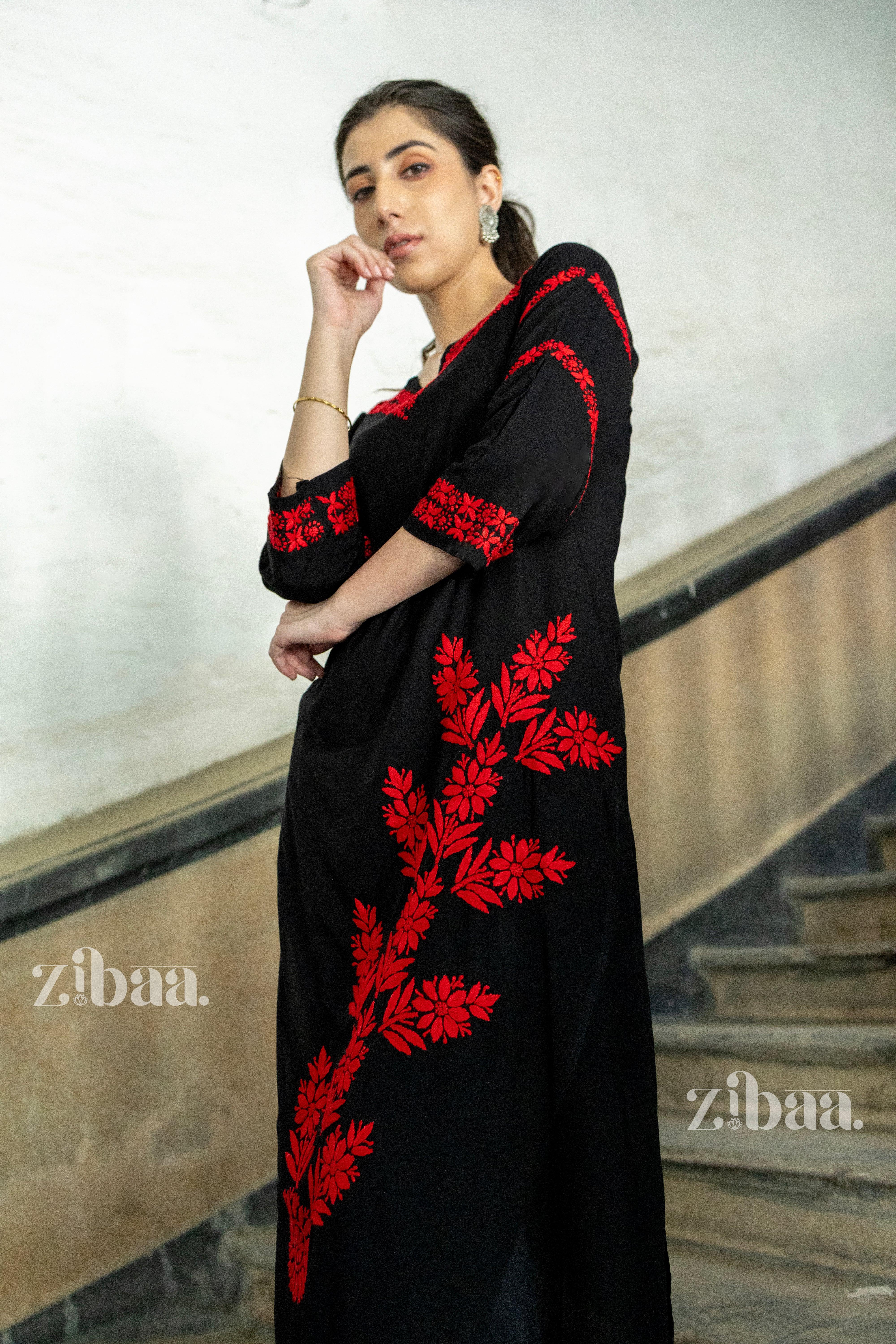 A woman posing in a black kurti with bold red floral embroidery, leaning on a staircase railing, styled with minimal jewellery.