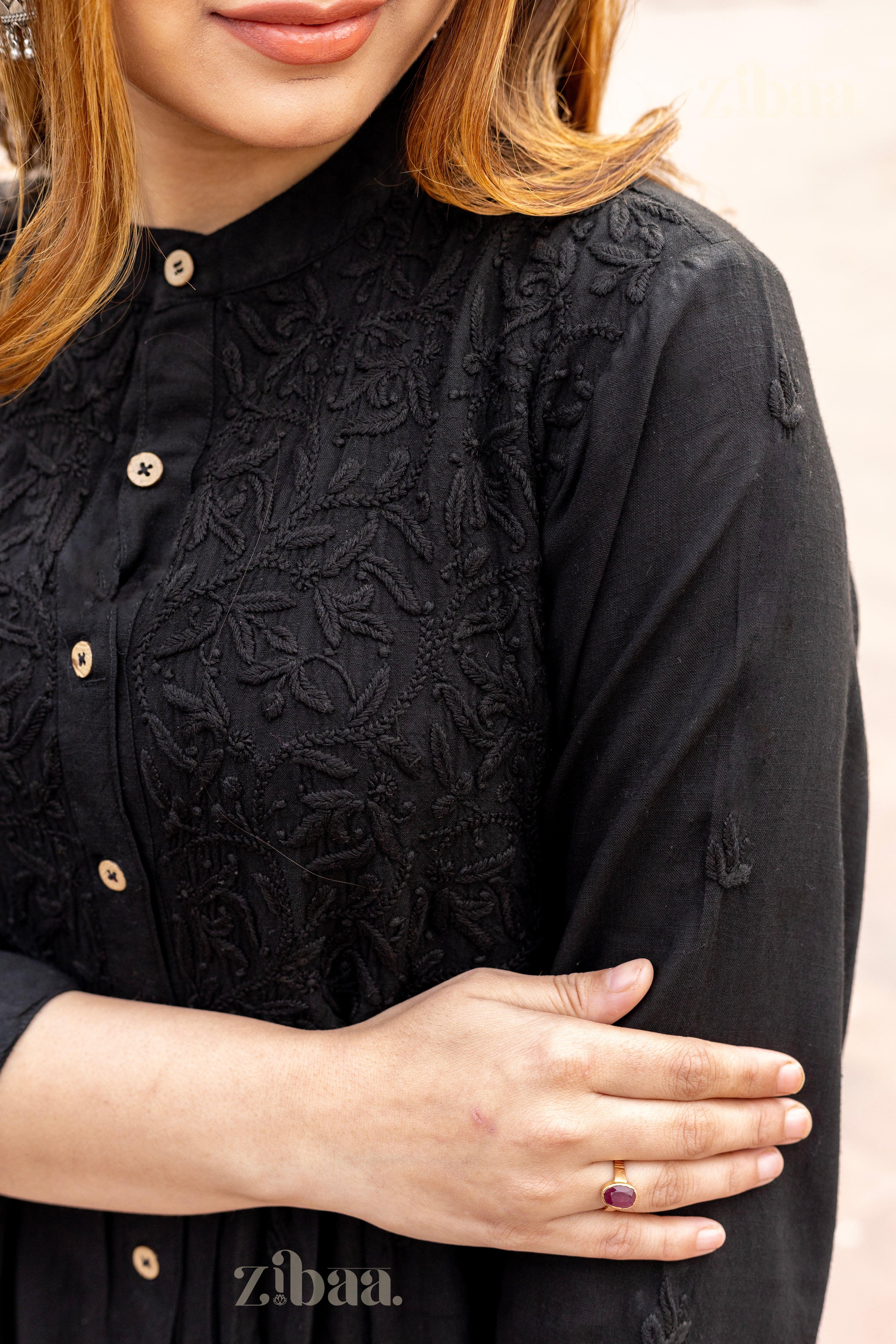 A close-up of a girl crossing her arms, showing intricate tonal embroidery and button-down detailing of a black Chikankari Kurti.