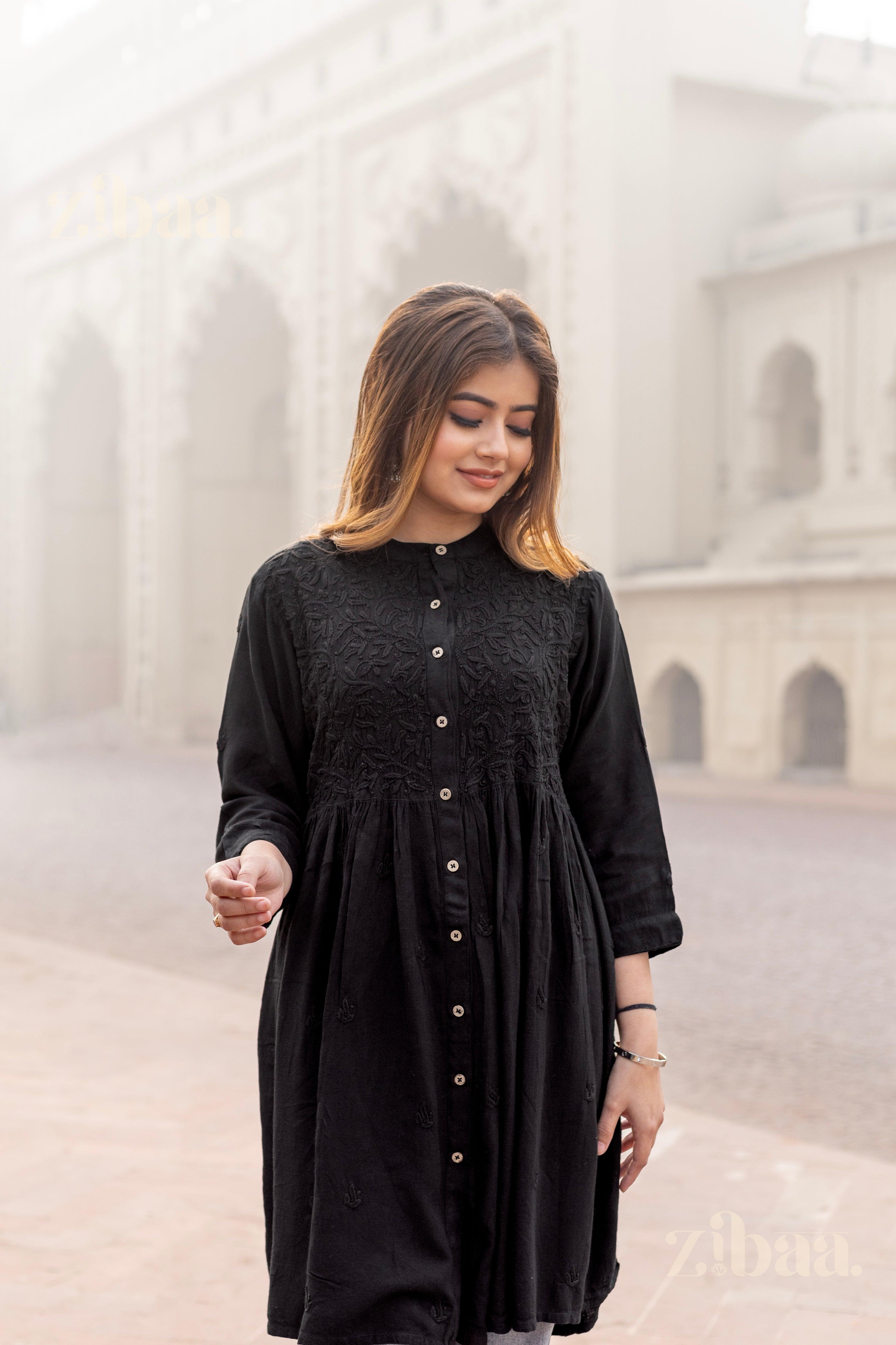 A woman walks in a serene outdoor setting, wearing a black Chikankari Kurti with intricate embroidery and button-down detailing.