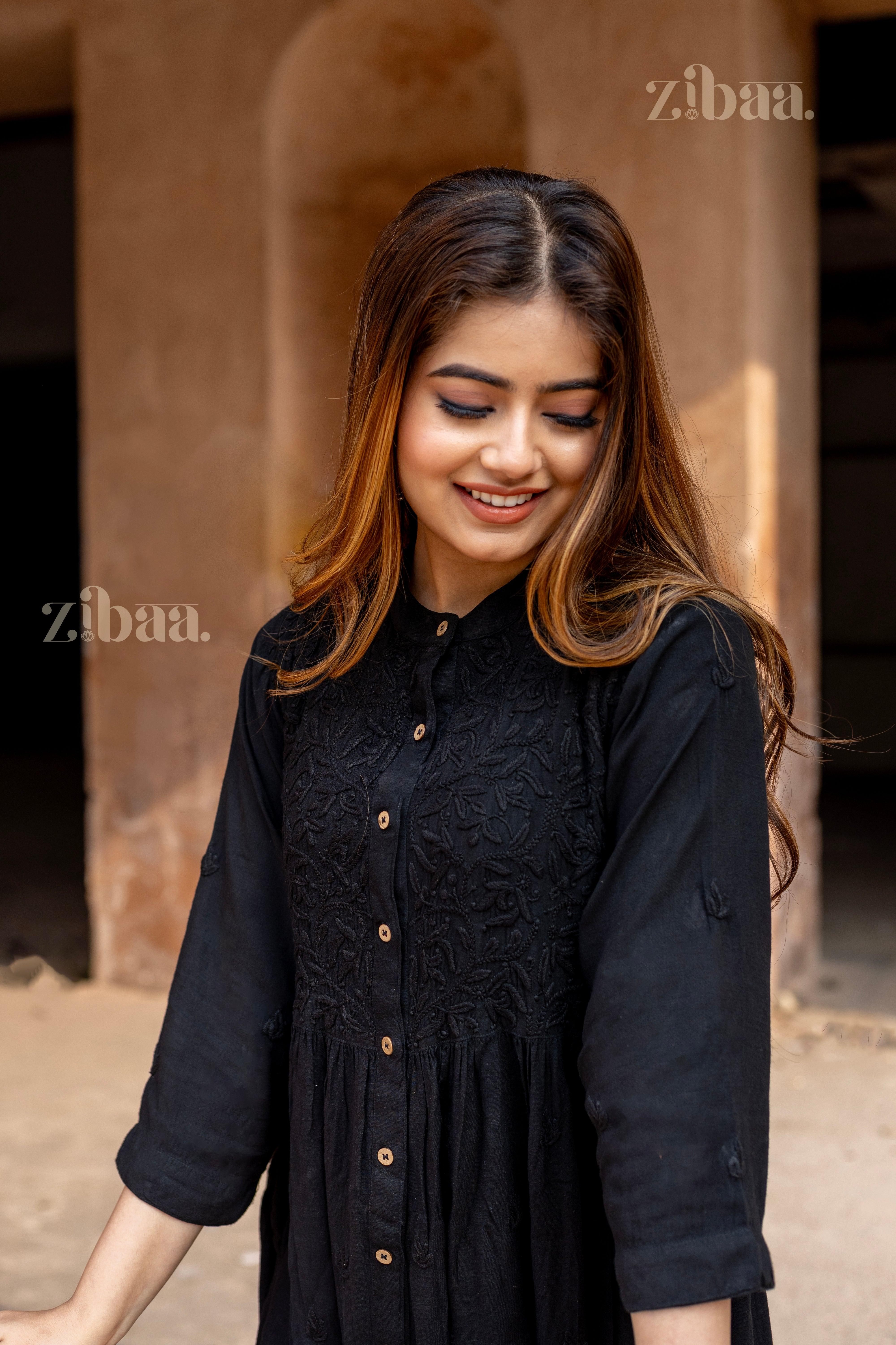 A woman smiles while tilting her head slightly, showing a black Chikankari Kurti with intricate embroidery and button-down details.