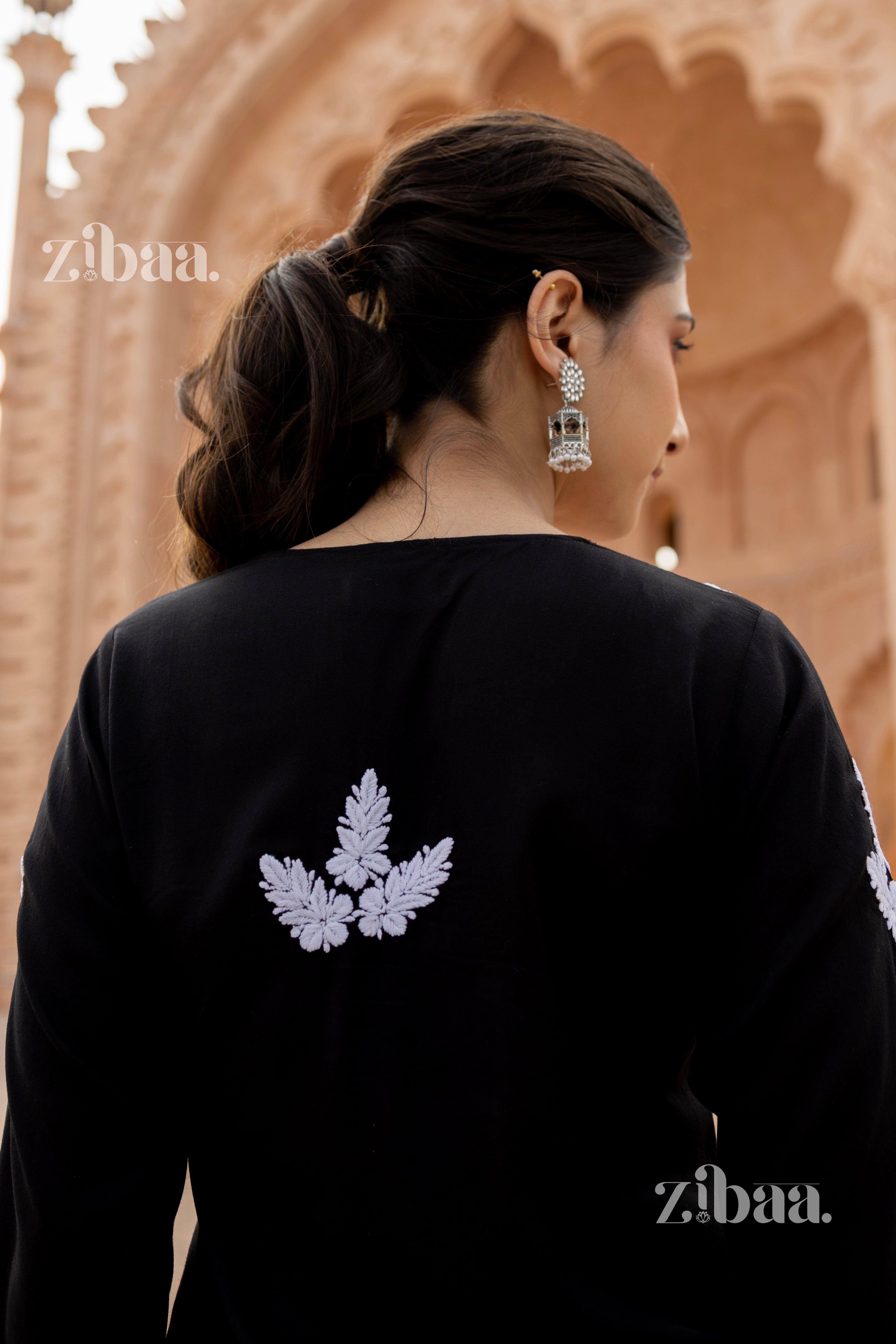 Back view of a girl in a black Chikankari kurti with white embroidered motifs, paired with statement earrings, in a heritage setting.