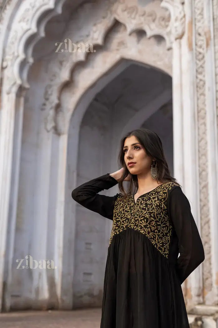 Model wearing a black Chikankari Kurti with gold embroidery, standing elegantly in front of a heritage architectural backdrop.