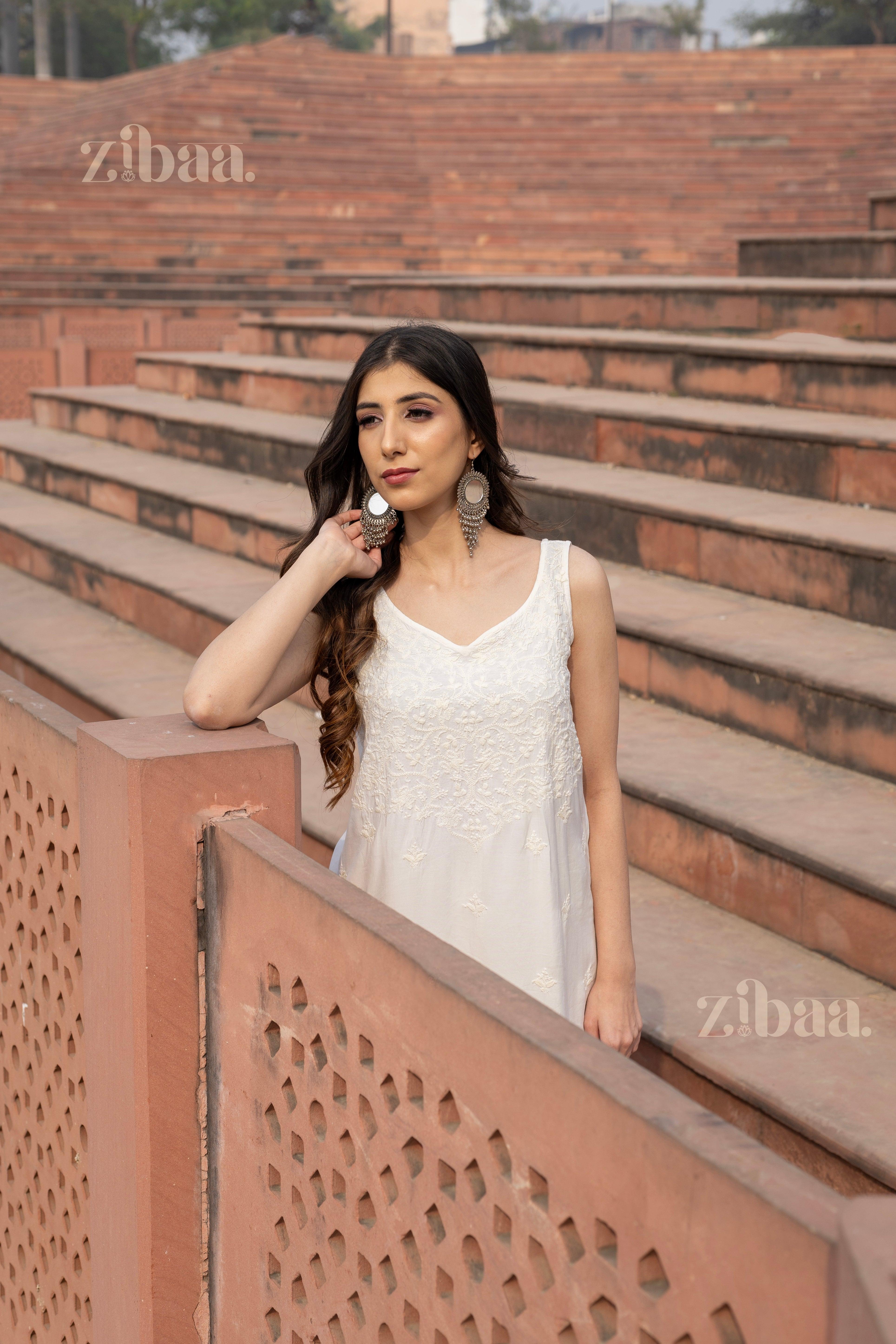 Model wearing a sleeveless white Chikankari kurti for women, posing elegantly against a traditional backdrop with intricate architecture