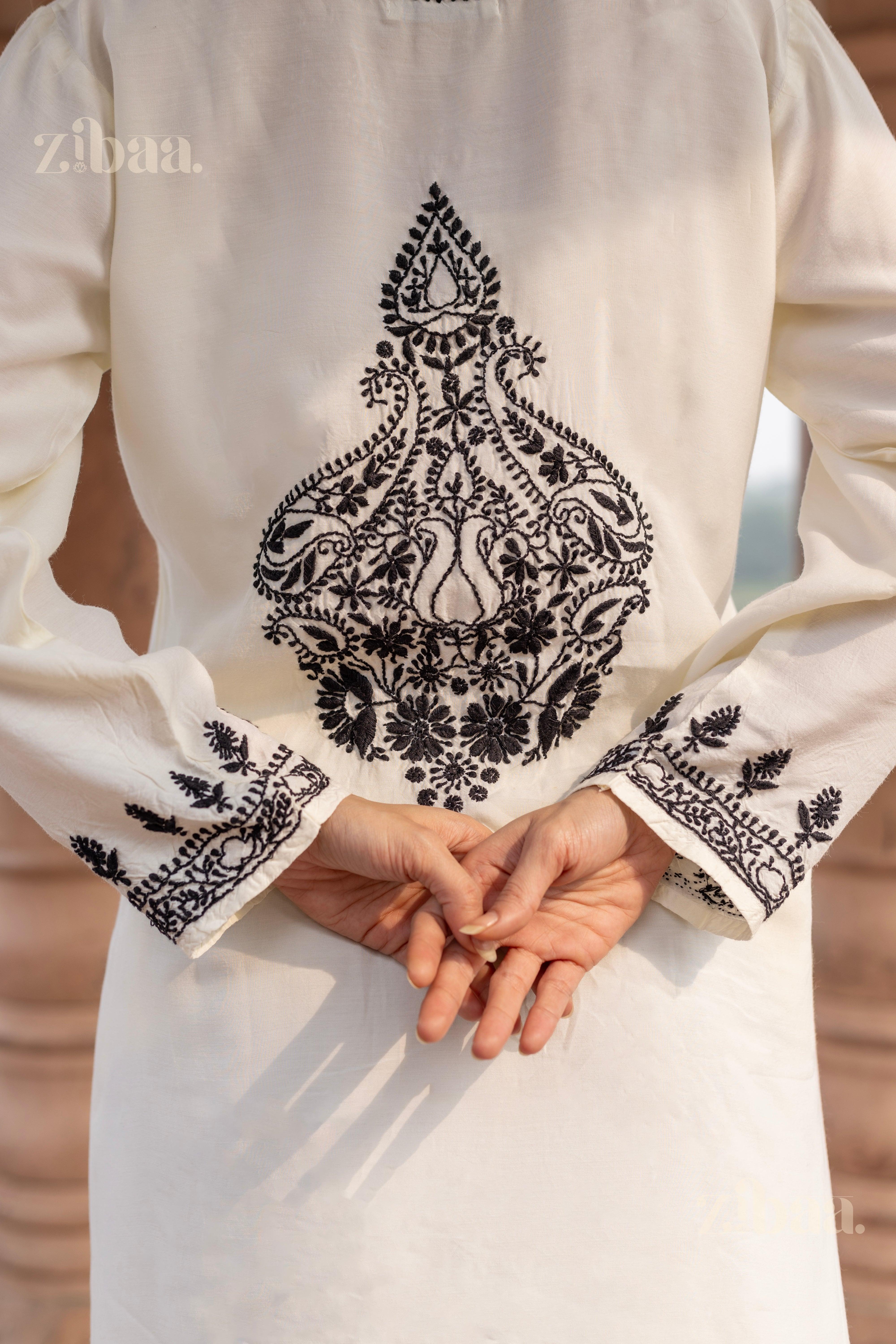 Back view of a white Chikankari kurta set with detailed black embroidery, as the woman clasps her hands behind her, standing outdoors.