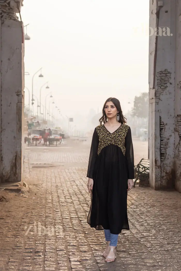 Full view of a Black Chikankari Kurti adorned with gold embroidery, styled with jeans, showing elegance in a rustic outdoor setting.