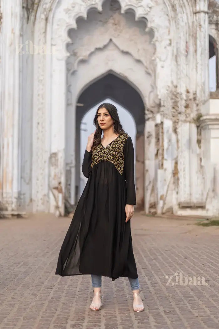 Full view of black Chikankari Kurti with gold embroidery, styled with jeans, set against a grand heritage architectural background.