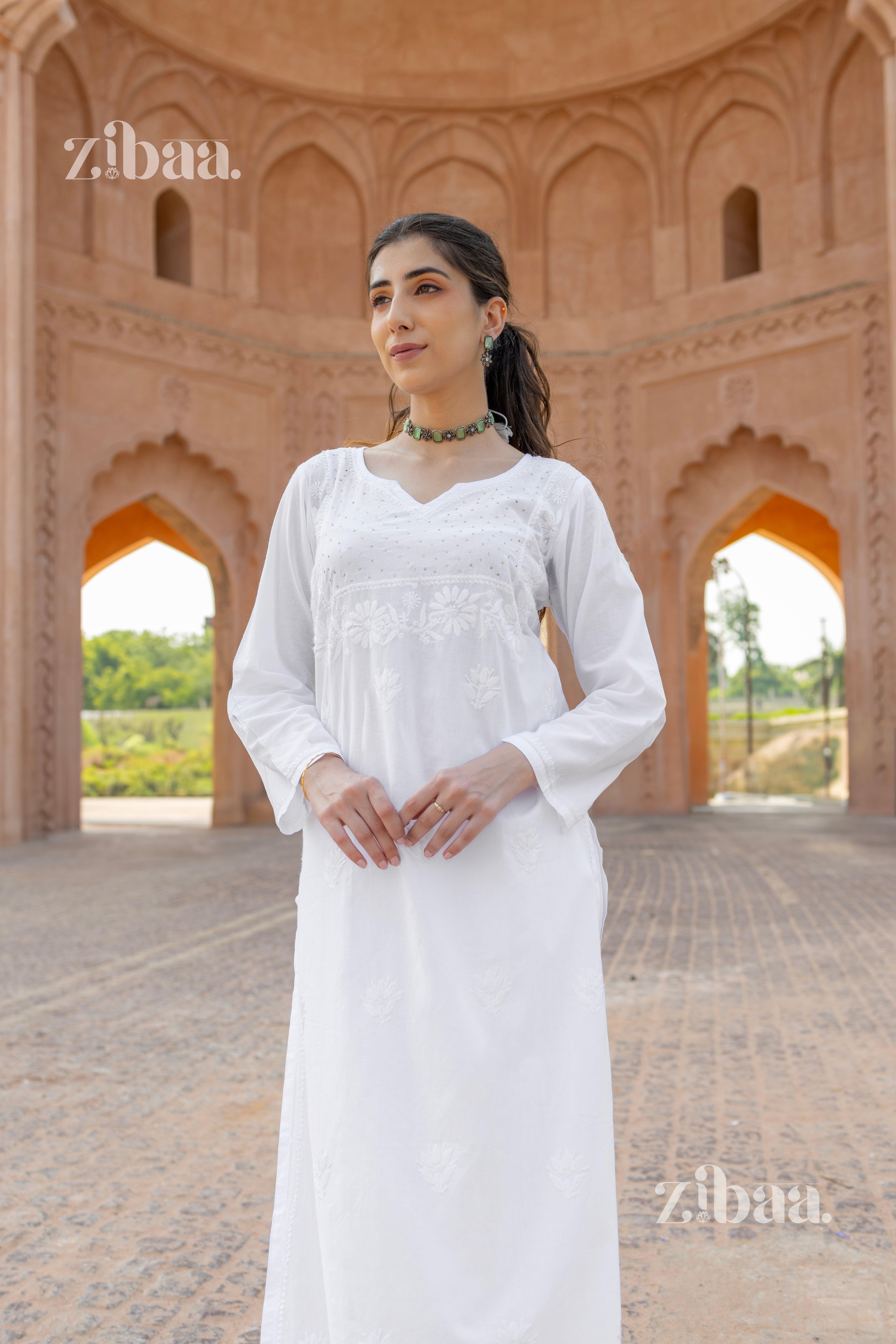 A woman posing in a white kurti for women with intricate Chikankari embroidery, styled with a choker necklace, in a heritage setting.