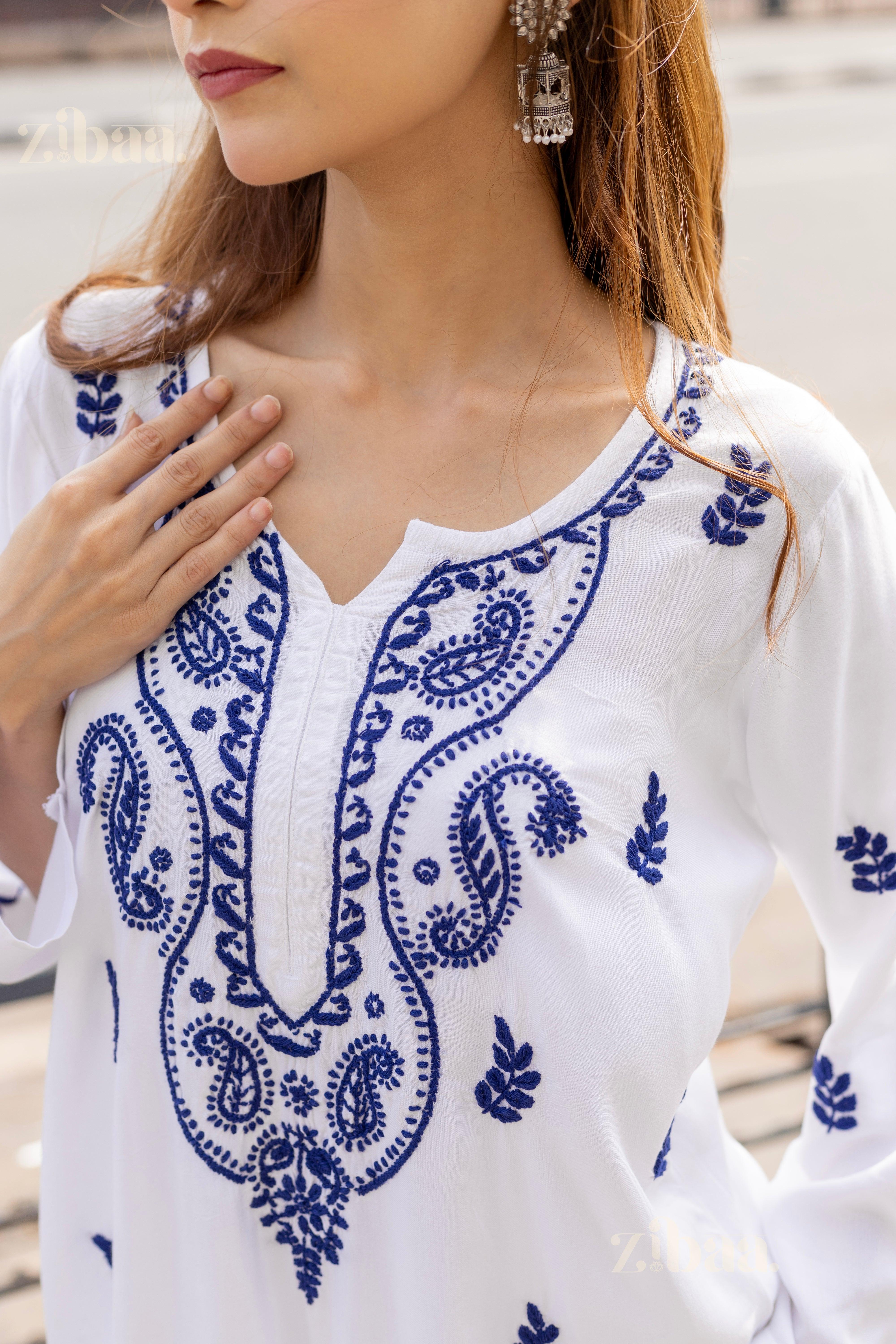 Close-up of a white Chikankari kurti showing intricate blue embroidery on soft fabric, styled with silver earrings in a chic look.