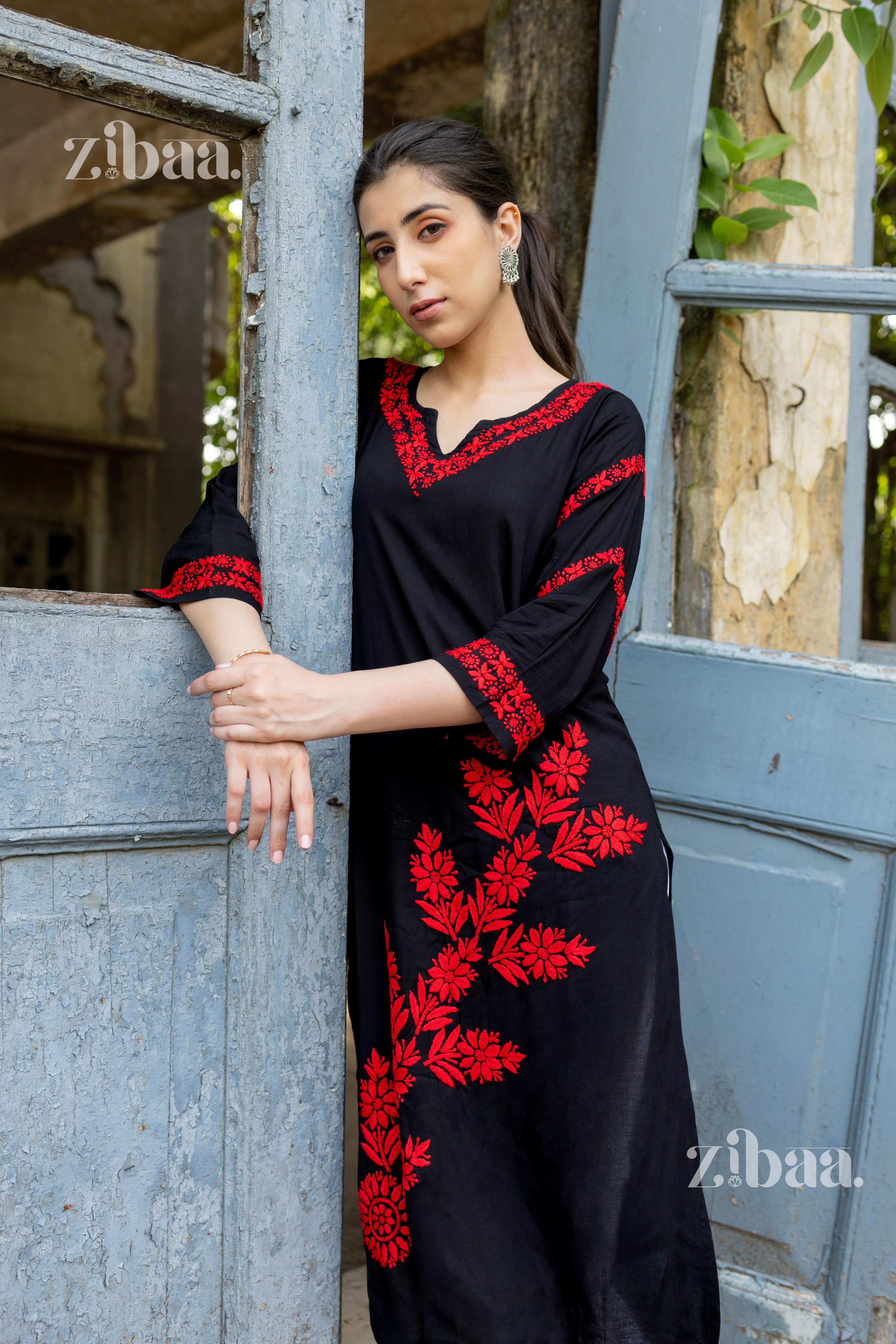 A girl posing in a black Chikankari kurti with bold red embroidery, styled with statement earrings, against a rustic backdrop.