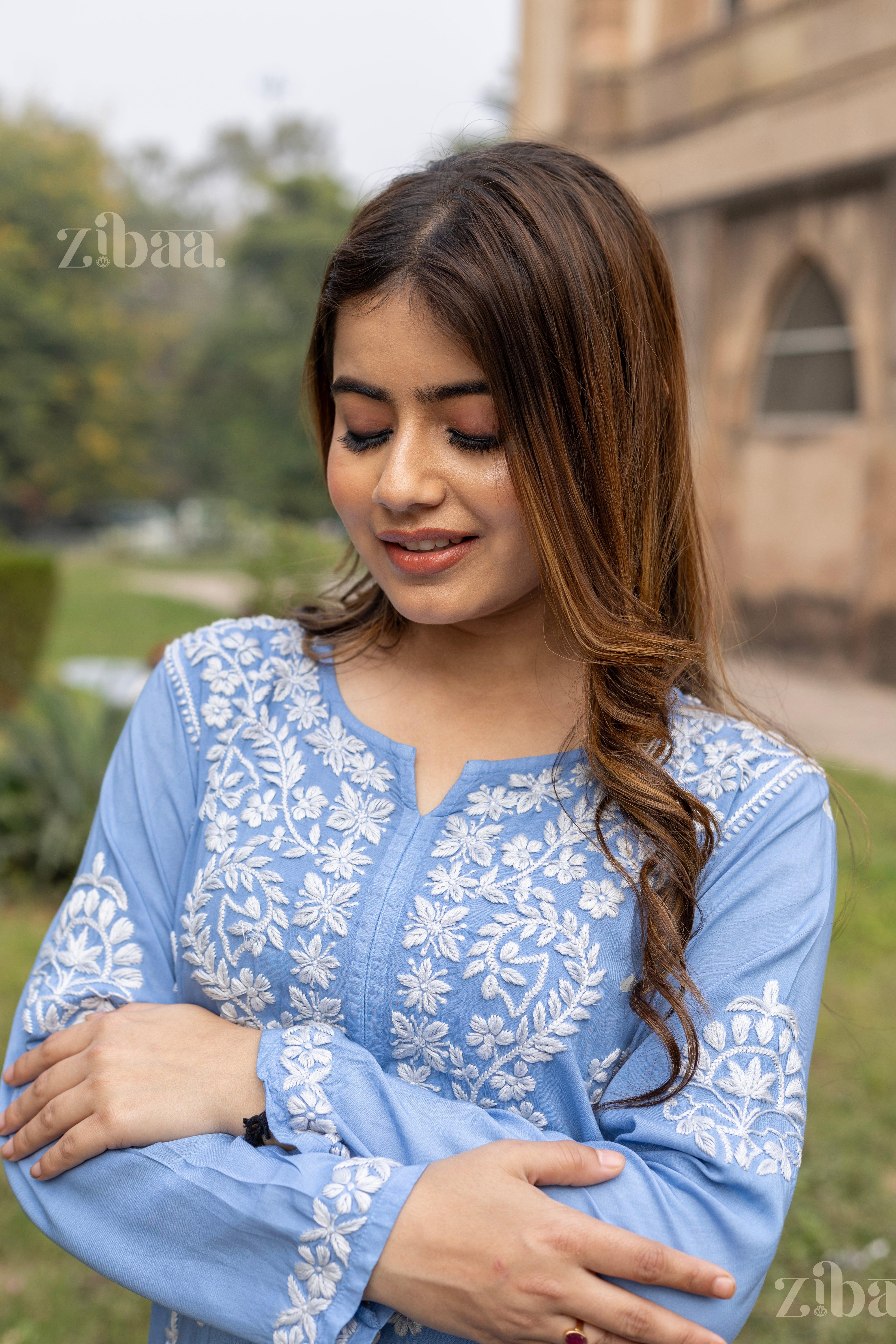 Model in a Blue Chikankari Kurta with white embroidery, smiling gracefully, showing intricate details in a beautiful outdoor setting.