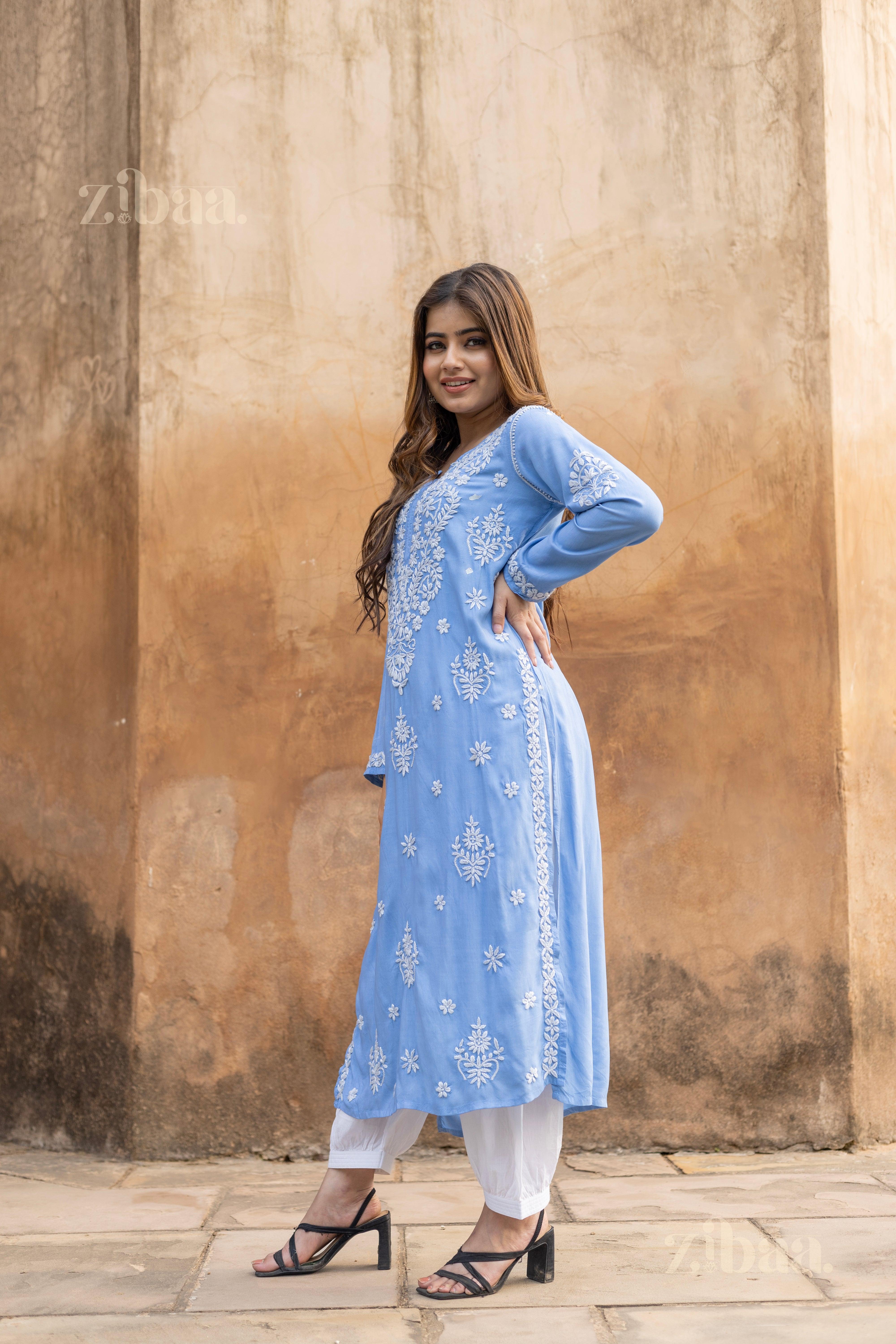 Model in Blue Chikankari Kurta with white embroidery styled with white pants shows grace against a rustic backdrop. 