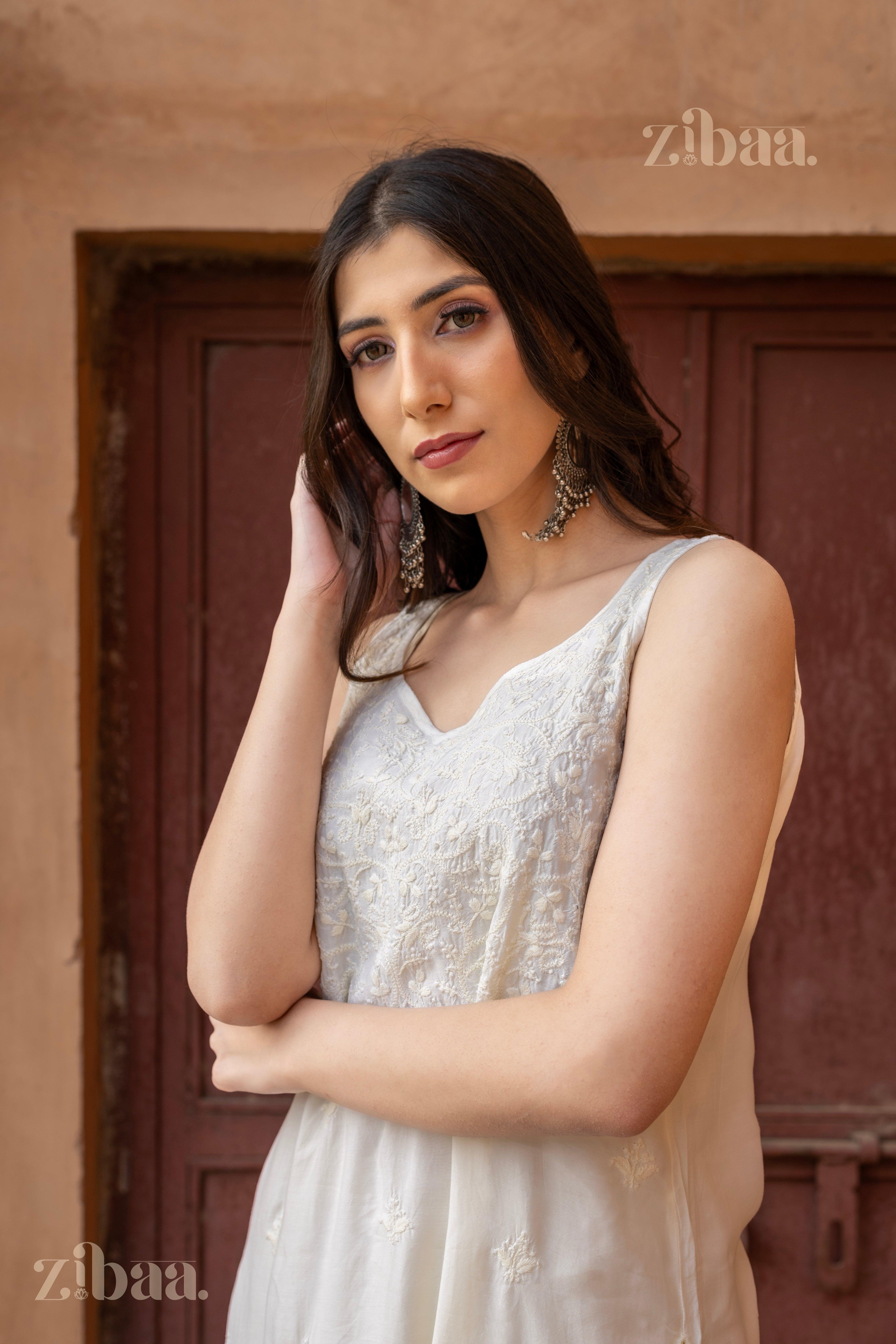 Model wearing a sleeveless white Chikankari Coord set, featuring intricate embroidery, posing gracefully in a rustic indoor setting