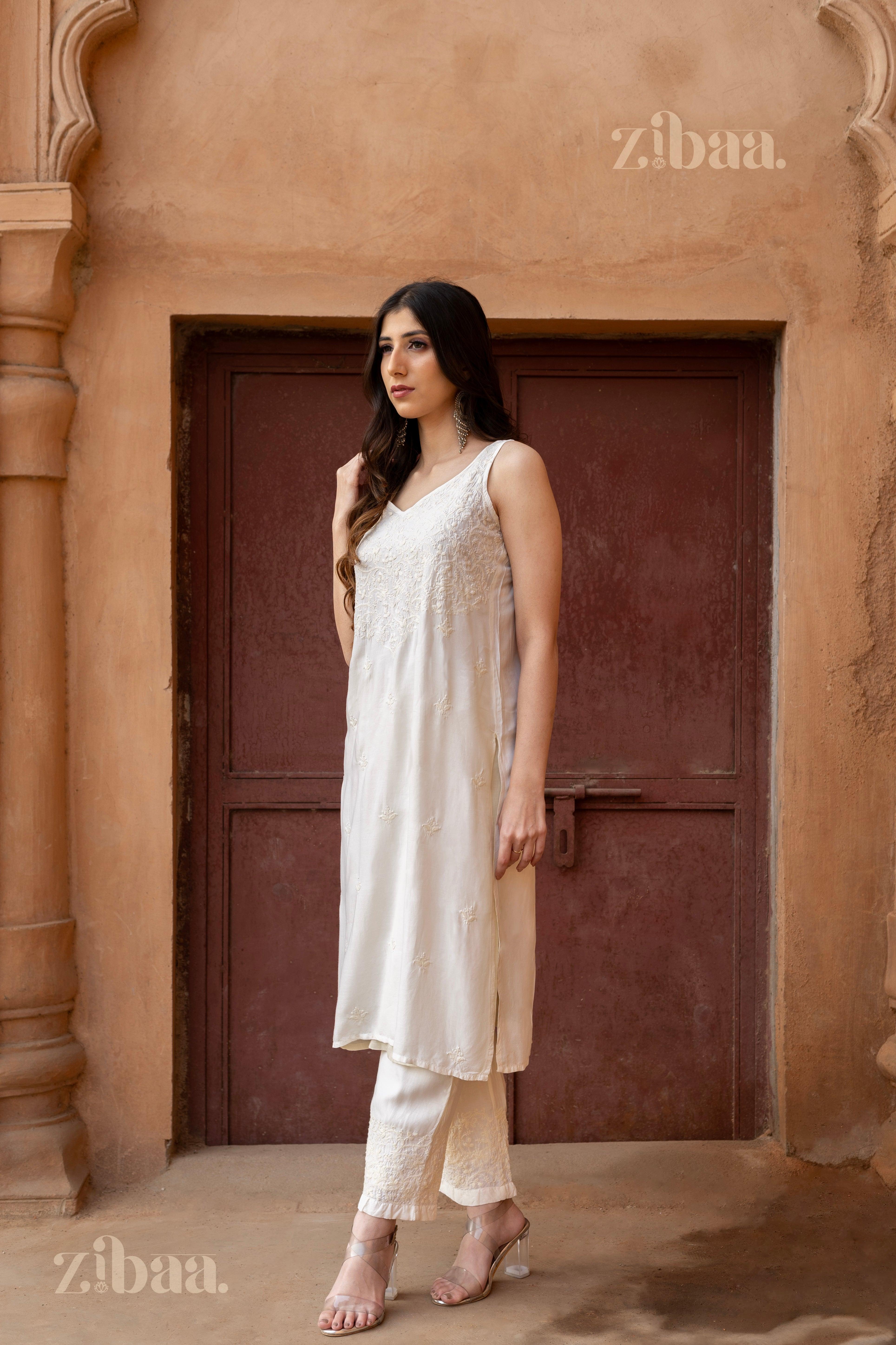 Model wearing a sleeveless White Chikankari Kurti with intricate embroidery, paired with matching pants, posing in a rustic setting