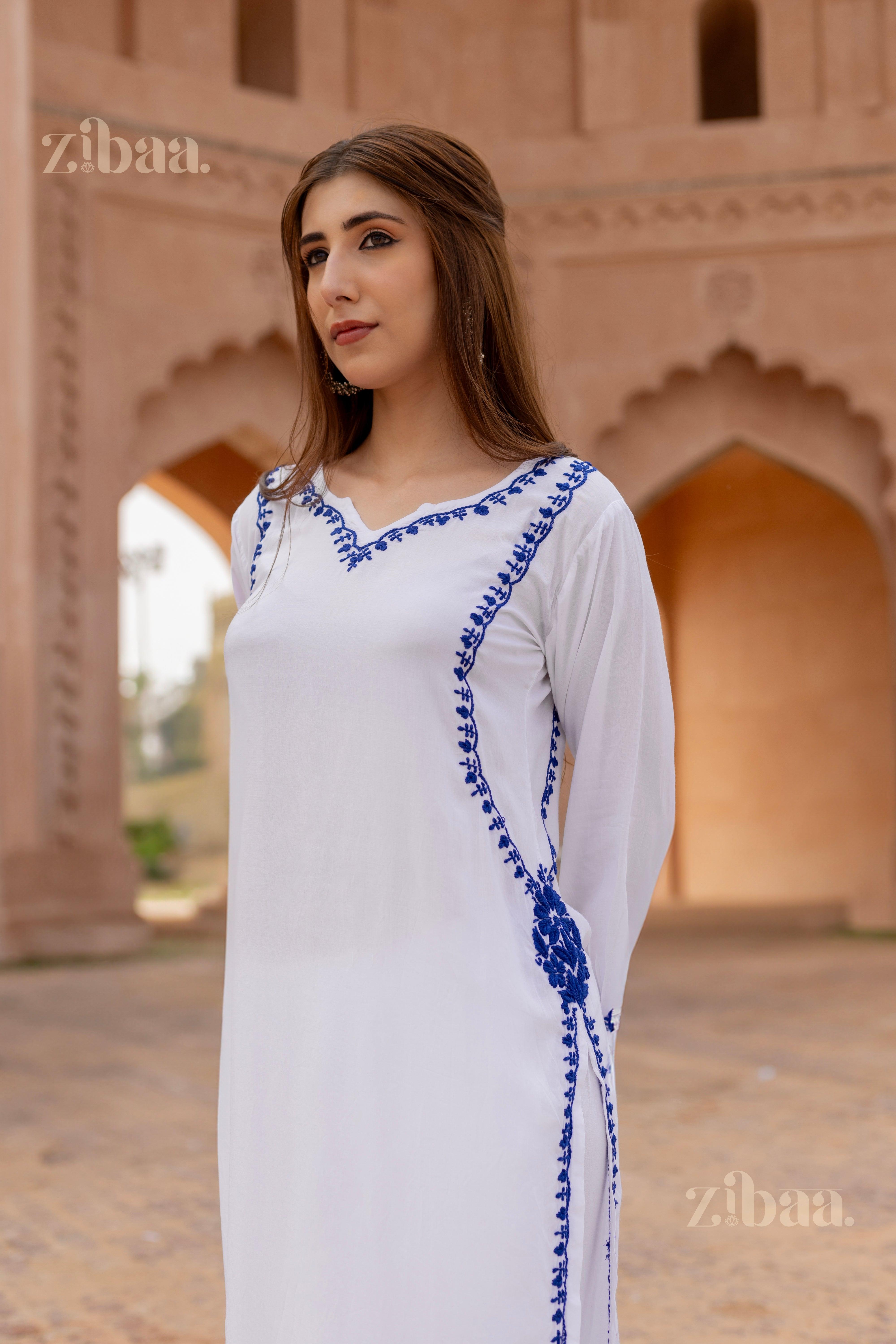 Woman standing in a white Chikan Kurti with intricate blue embroidery, posing outdoors against a heritage architectural backdrop