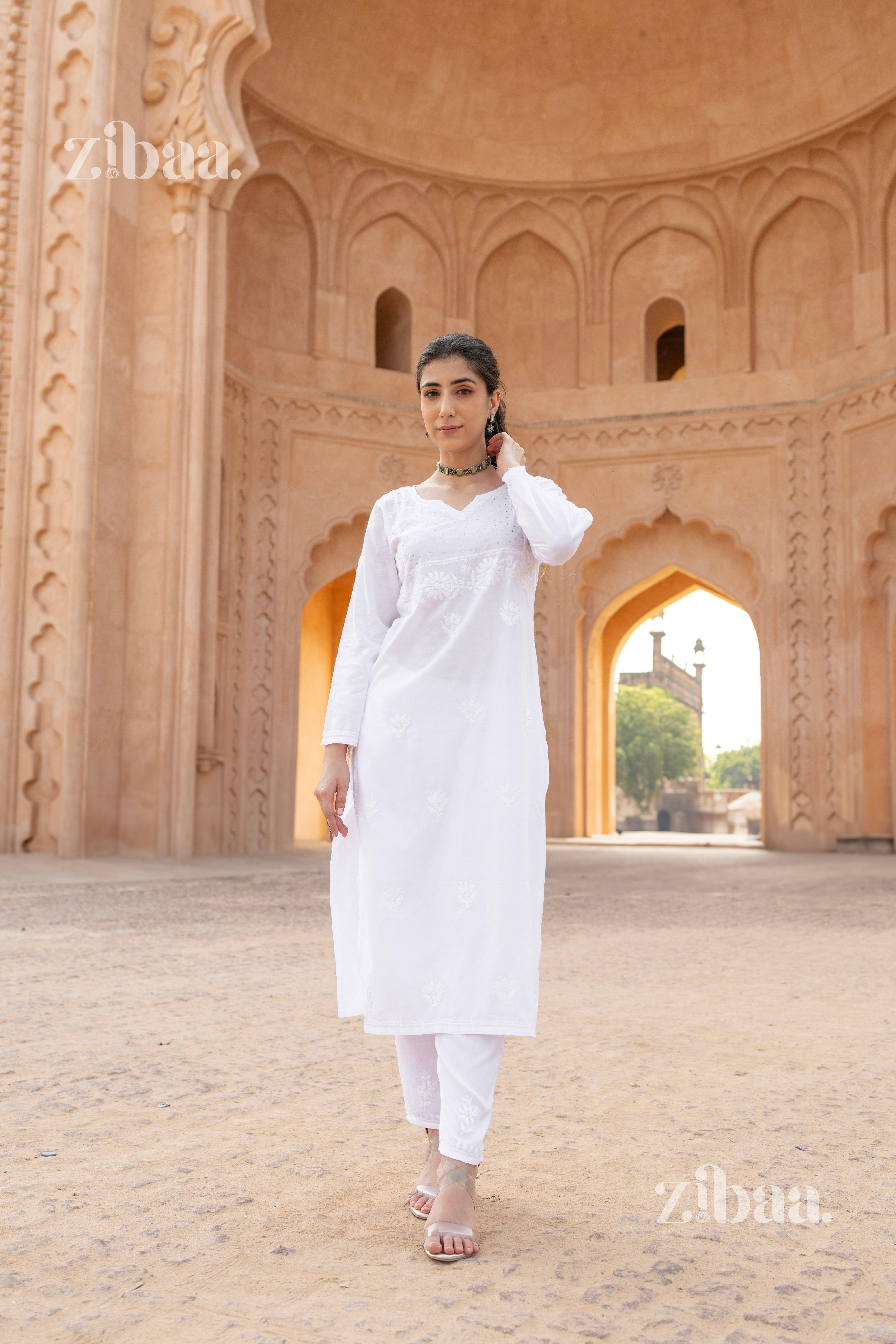 A woman walking in a white chikan kurti with intricate embroidery, paired with white pants and heels, in a heritage-inspired setting.