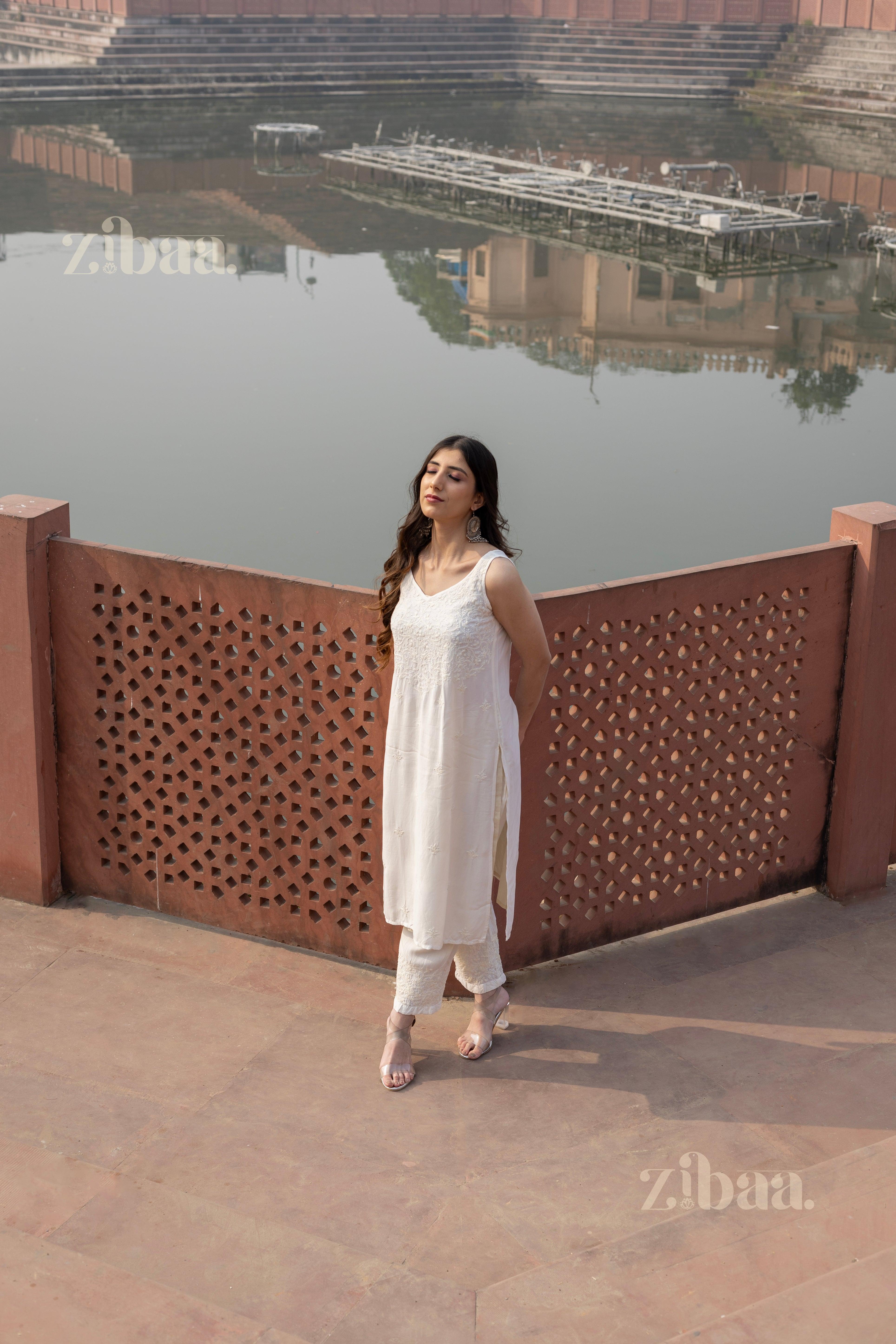 Model in a white Chikankari Kurta Set with intricate embroidery, posing gracefully near a serene lakeside architectural backdrop