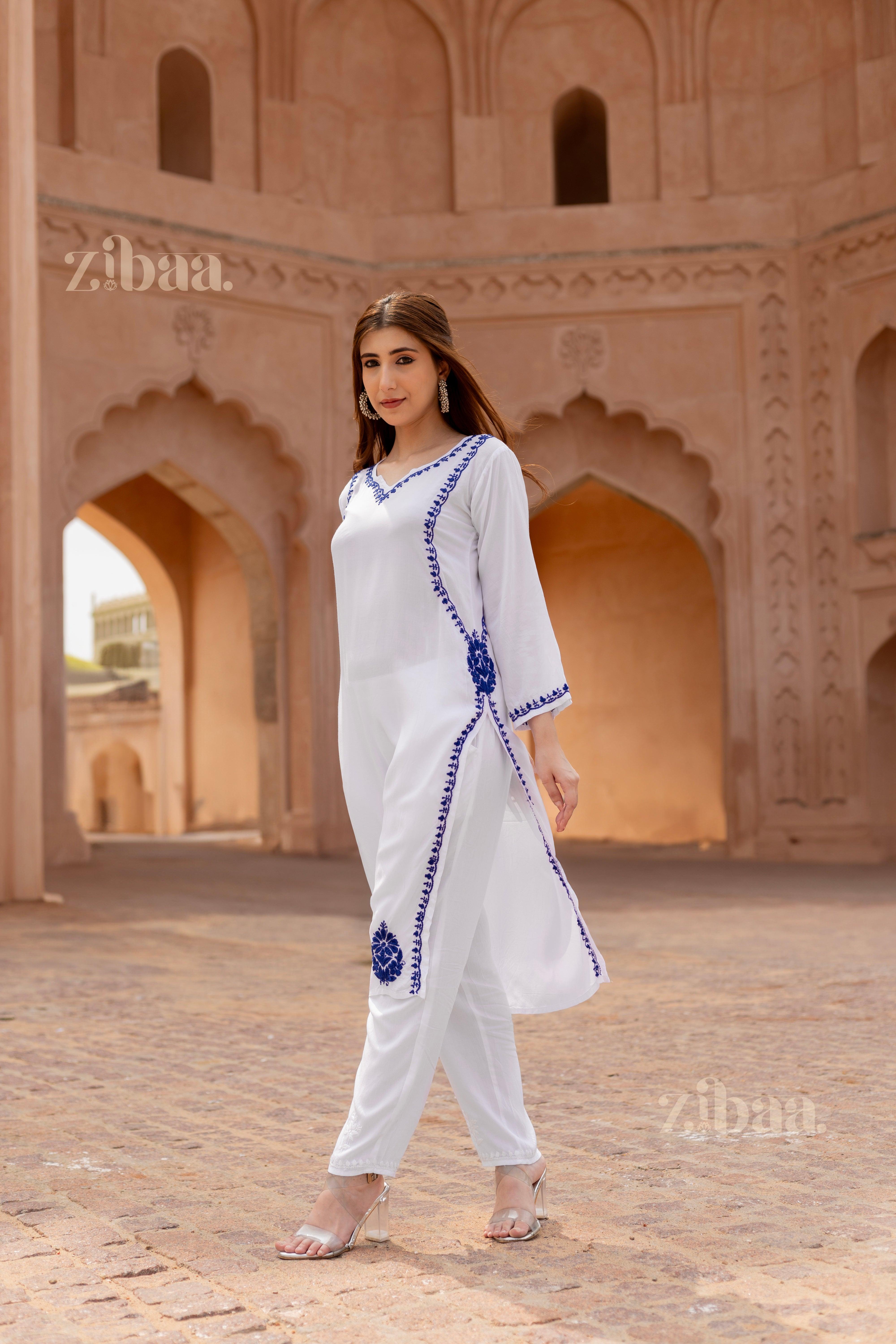 Girl wearing a white kurti for women with intricate blue embroidery on the neckline, gracefully posing outdoors in a serene setting