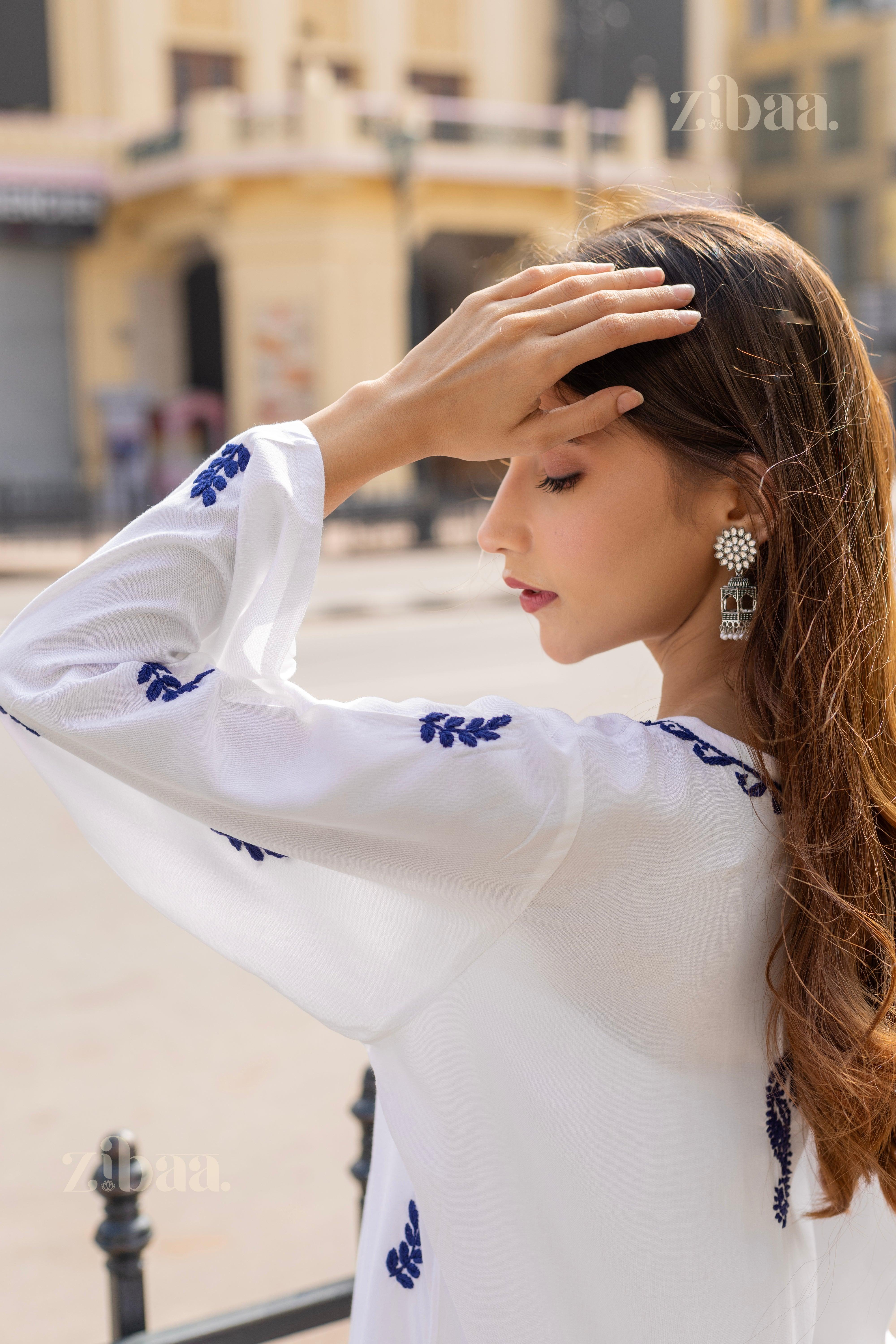 Side profile of a girl in a white Chikankari Kurti with fine blue embroidery, styled elegantly with statement earrings outdoors.