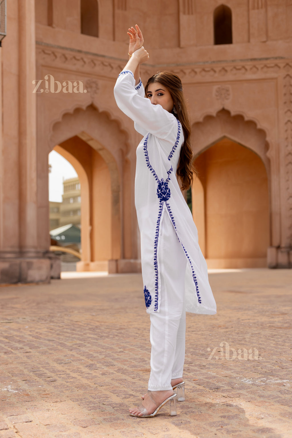 Close-up of a woman showcasing a white kurti for women with intricate blue floral embroidery, pointing to the detailed side design