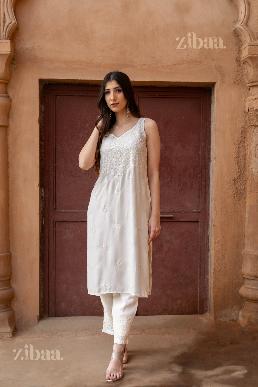 The Chikankari kurta set the model wears has an elegant pose in front of a historic monument, which is located in an outdoors setting.