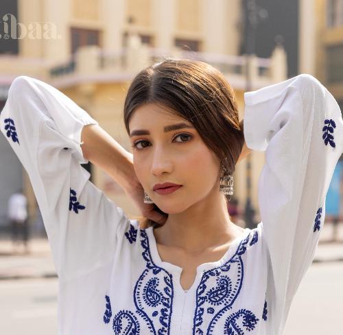 Stylish pose in a white Chikankari Kurti featuring intricate blue embroidery, blending elegance and tradition in an outdoor setting.